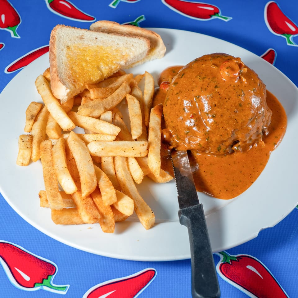 Plate of fries, toasted bread, and a burger covered in creamy orange sauce on a chili pepper-patterned tablecloth.