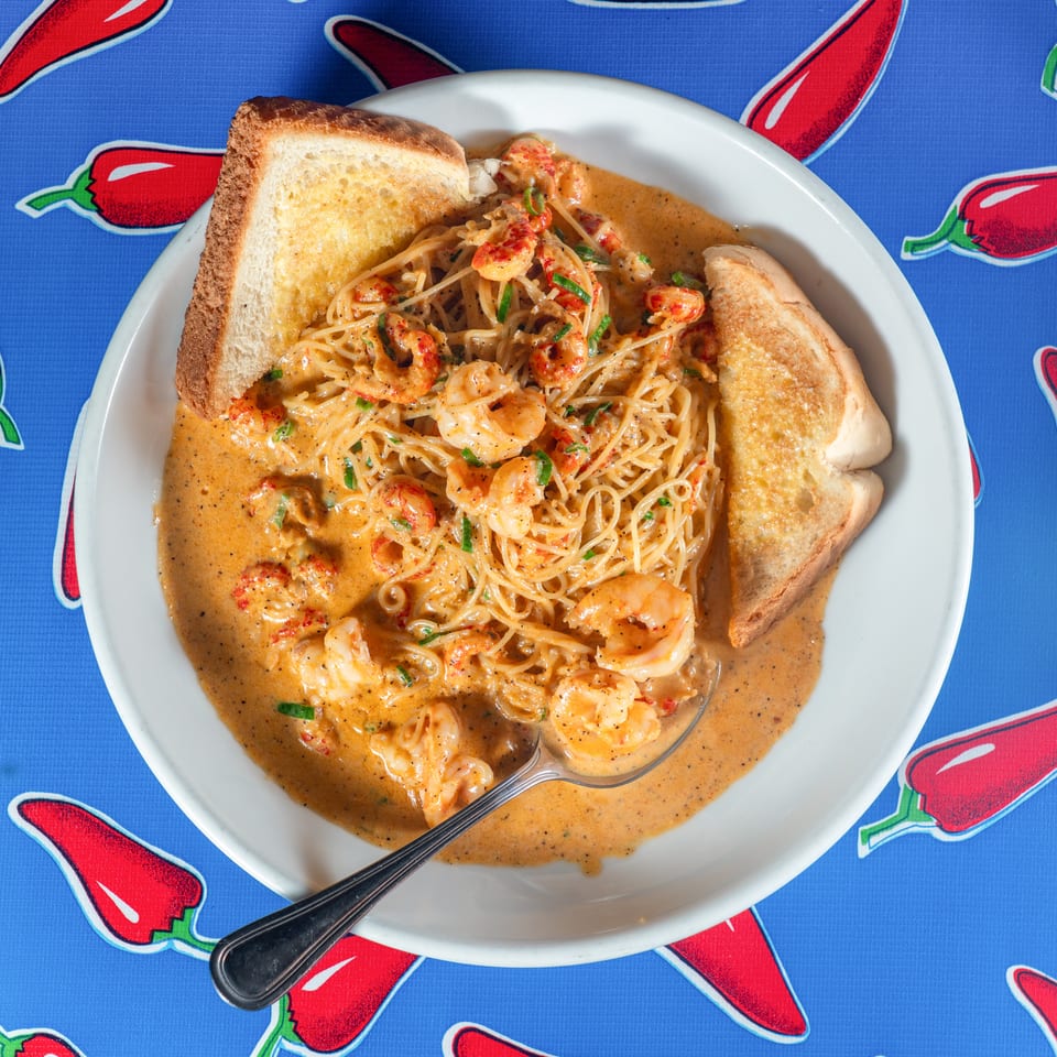 Creamy shrimp spaghetti with garlic toast served on a white plate over a red chili pepper patterned tablecloth.