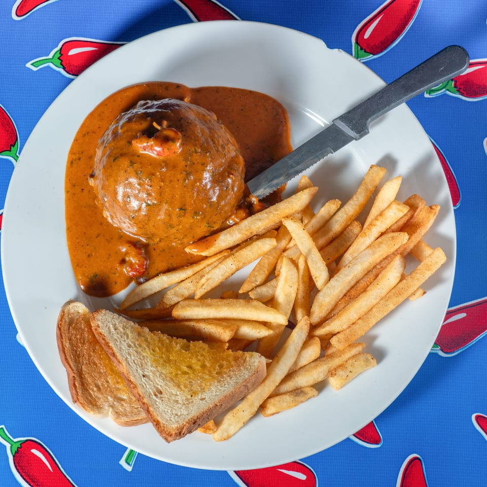 Plate of meat covered in creamy brown sauce with French fries and toast on a red chili pepper patterned tablecloth.